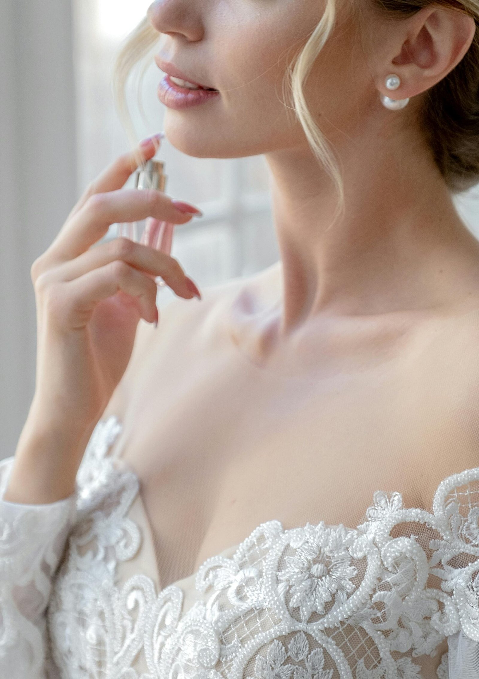 Close-up of a woman elegantly applying perfume wearing a beautiful lace dress.